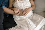 couple sitting on couch with hands over female partner's pregnant belly - what to expect before you're expecting WeNatal